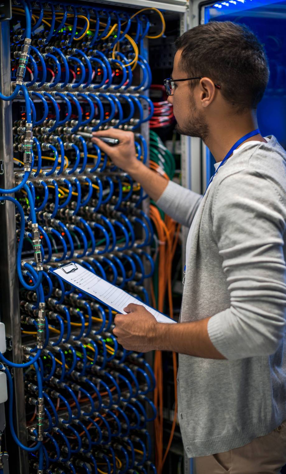 Back view portrait of young man connecting wires in server cabinet while working with supercomputer in data center